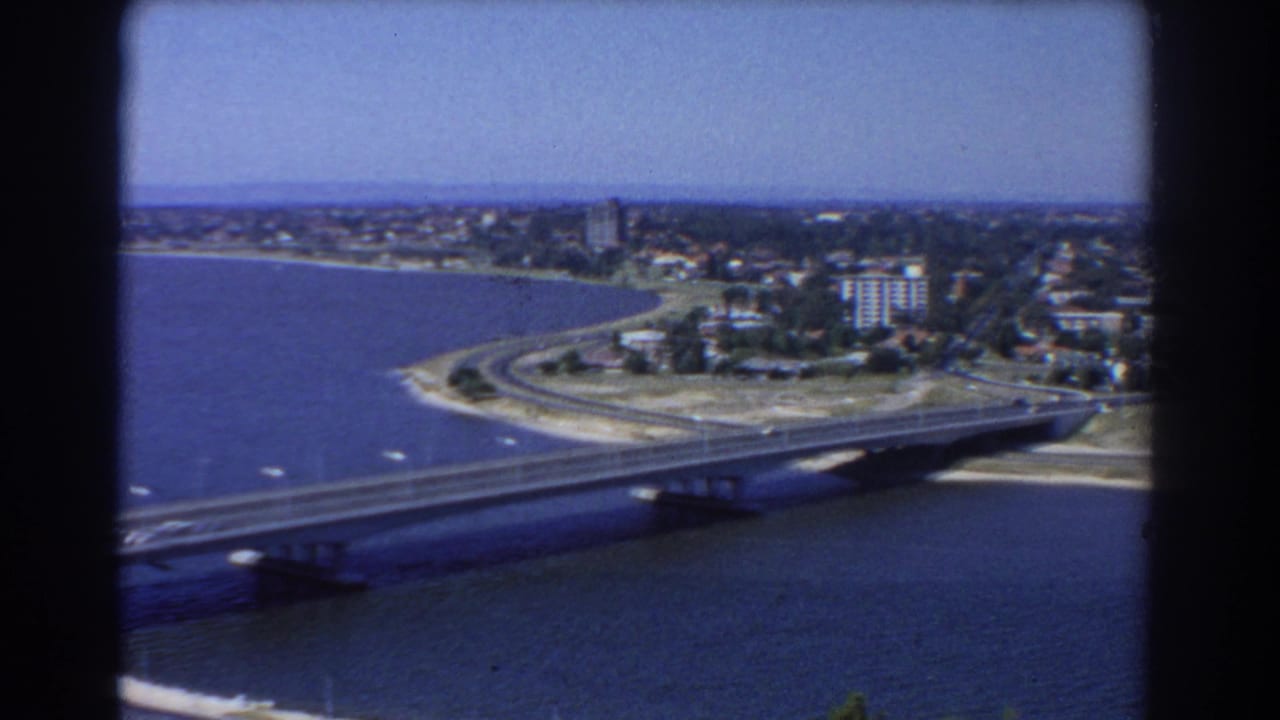Elevated view of a bridge crossing blue water toward a built-up shoreline.