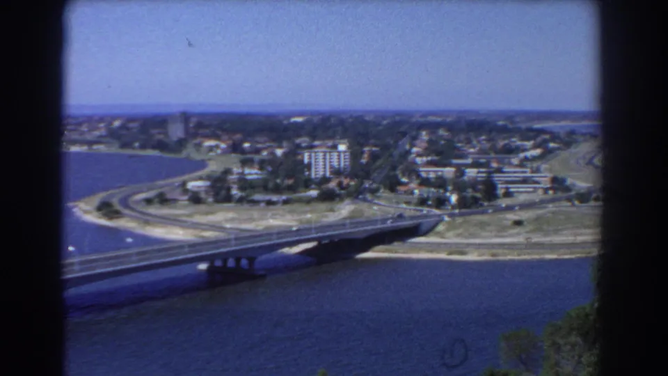 1967 Perth waterfront with a bridge, roads, cars, open shoreline, low-rise blocks, and a few taller buildings beyond the water.
