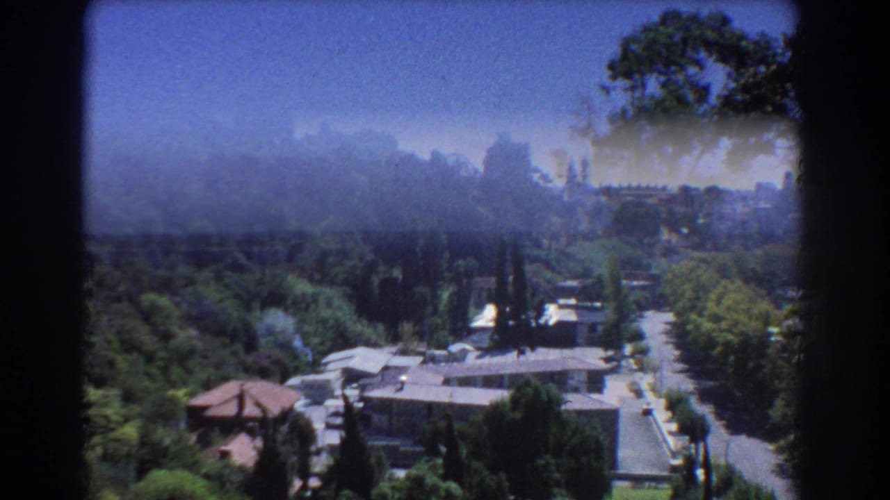Soft 8mm view over trees, rooftops, and a road toward a hazy Perth hillside skyline.
