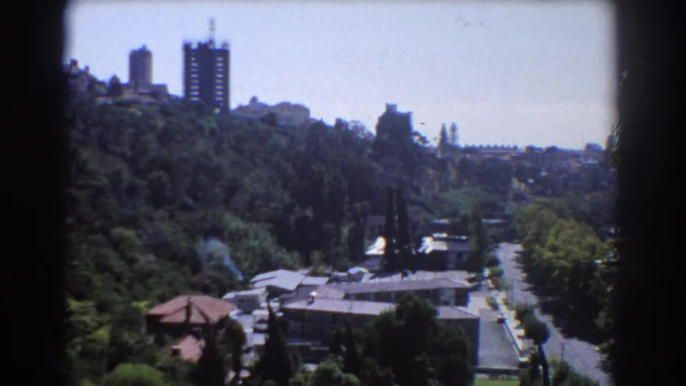 1967 Perth city vista from a high viewpoint, showing hillside greenery, low buildings, a road, and distant towers.