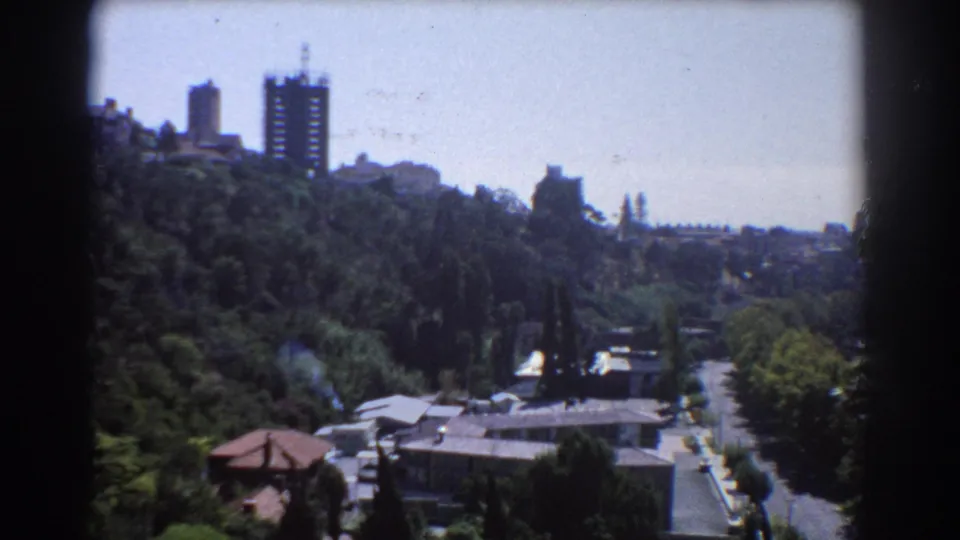 1967 Perth 8mm frame showing a hillside skyline, dense trees, residential rooftops, and a road in the foreground.