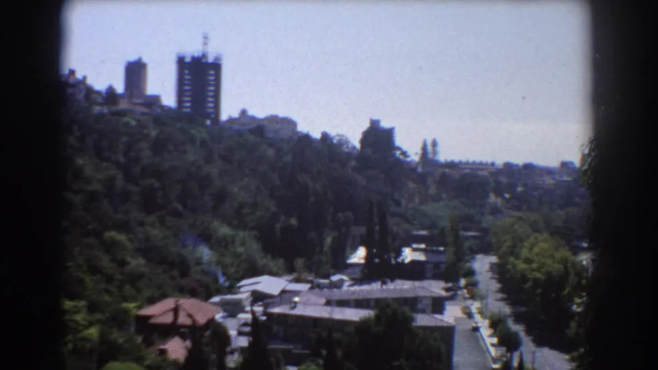 1967 Perth home-movie view across trees and rooftops toward distant high-rises, with visible 8mm frame edges.