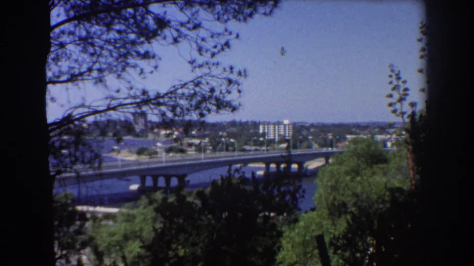 1967 Perth river-and-bridge view with dark foreground trees and soft 8mm color across the skyline.