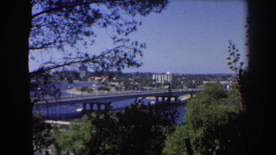 Final 1967 Perth frame showing the river bridge and distant urban development through leafy foreground shadows.
