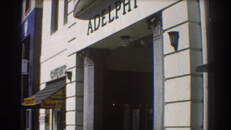 1967 Perth close view of a building facade with large ADELPHI lettering, an entrance, wall lamps, and a shop awning below.