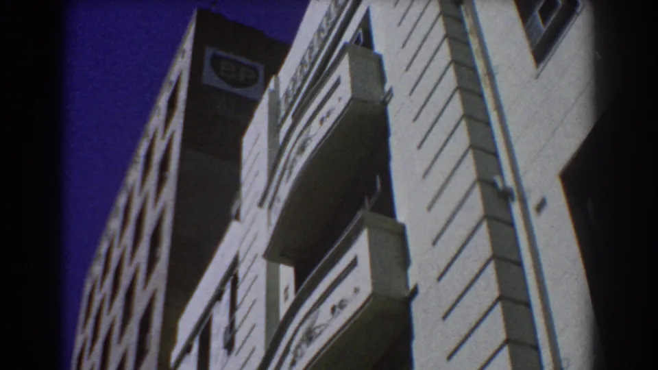 1967 Perth home-movie frame showing sunlit city buildings from below, with balconies and a visible BP sign near the roofline.