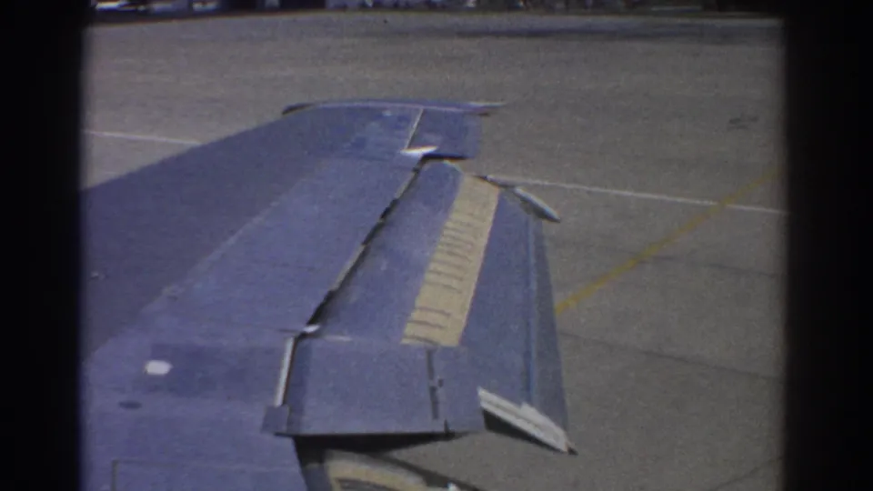 1967 Perth travel frame showing a blue aircraft wing with flaps visible over a bright airport tarmac.