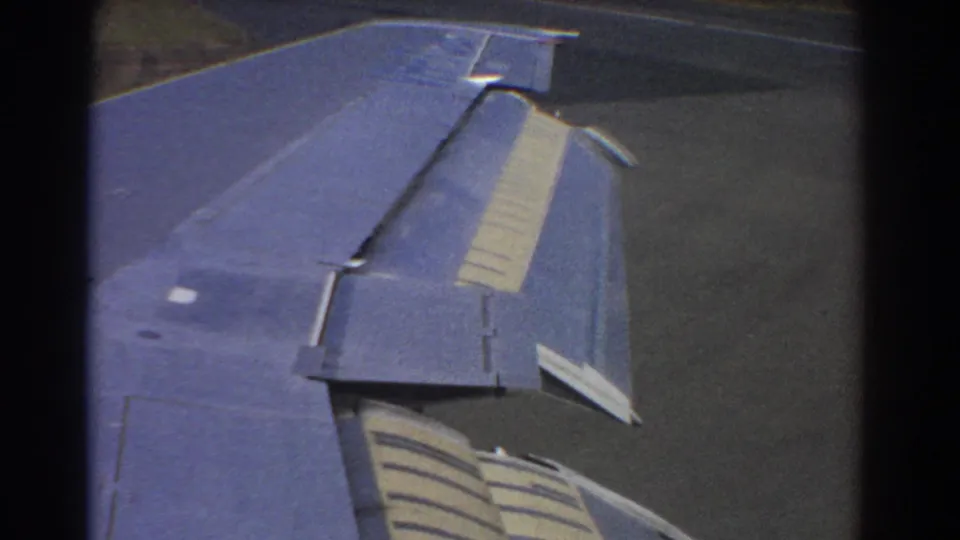 Passenger-window view of the aircraft wing in Perth, 1967, with flap details visible above the airport pavement.