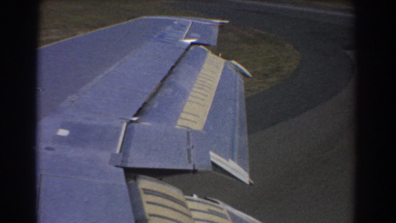 Blue aircraft wing seen from a passenger window during descent over runway and grass.