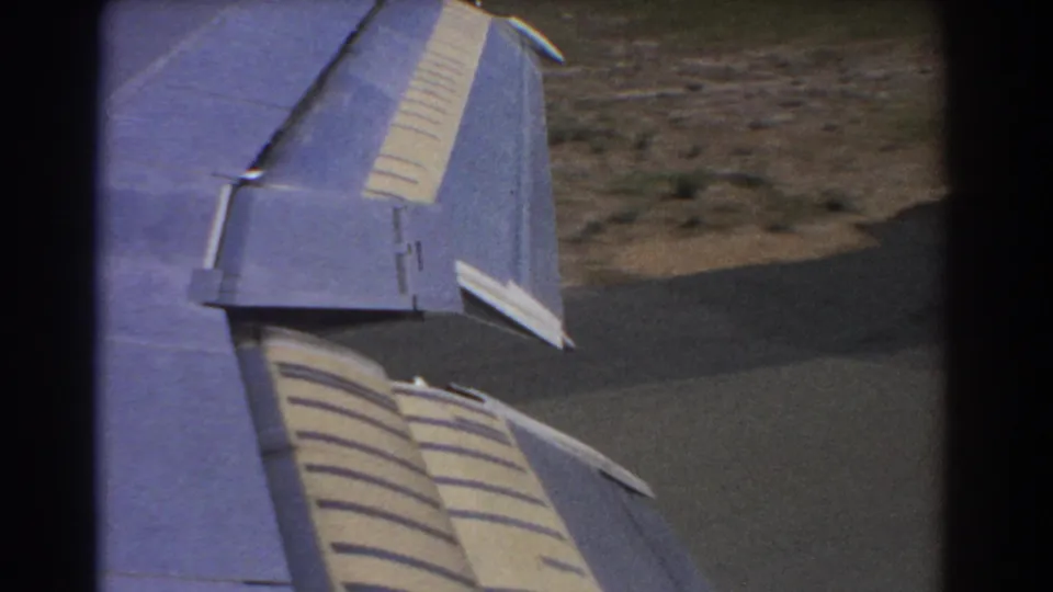 8mm home-movie view of a blue aircraft wing during descent, with runway and airport ground below in Perth, 1967.