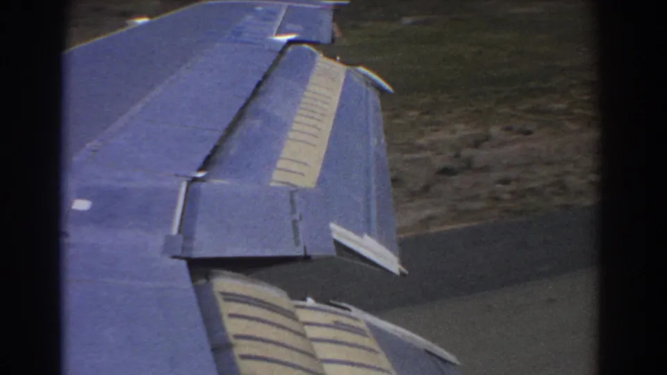 Passenger-window frame from 1967 Perth showing the aircraft wing, flaps, runway, and surrounding airport terrain.