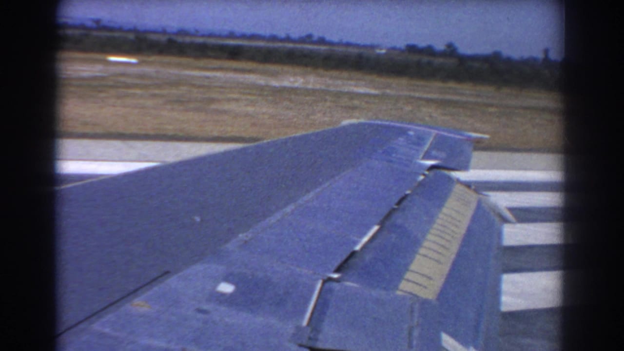 Airplane wing seen from a passenger window beside runway pavement and open ground.