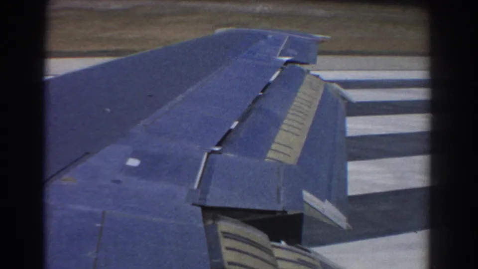 1967 Perth home-movie frame looking across the aircraft wing and flaps toward runway markings during ground movement.