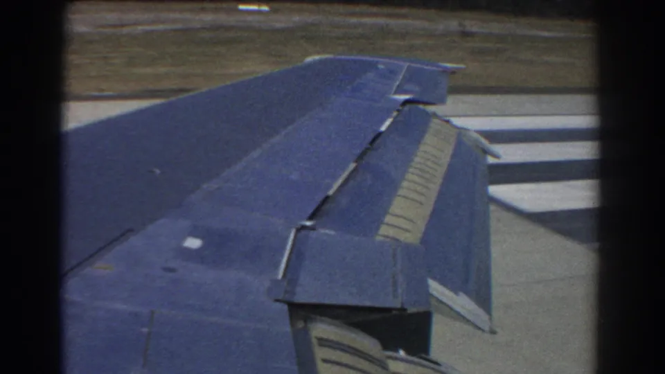 Passenger-window view from the 1967 Perth clip showing the airplane wing, flap assembly, and runway surface.