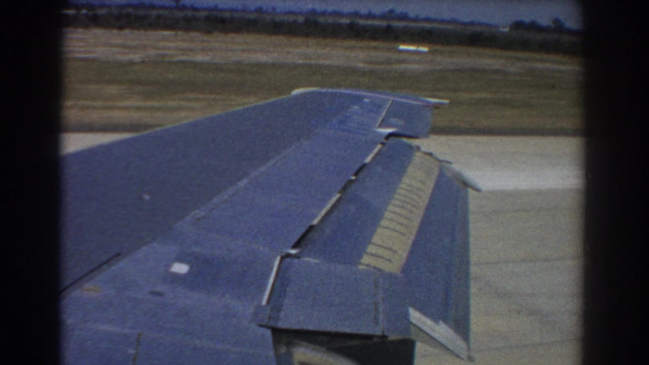 Right airplane wing with flap detail above runway and grassy field.
