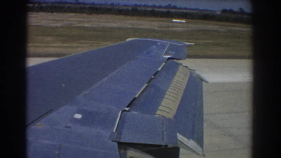 Blue right wing of an aircraft in 1967 Perth footage, with flap detail visible over runway and grass.