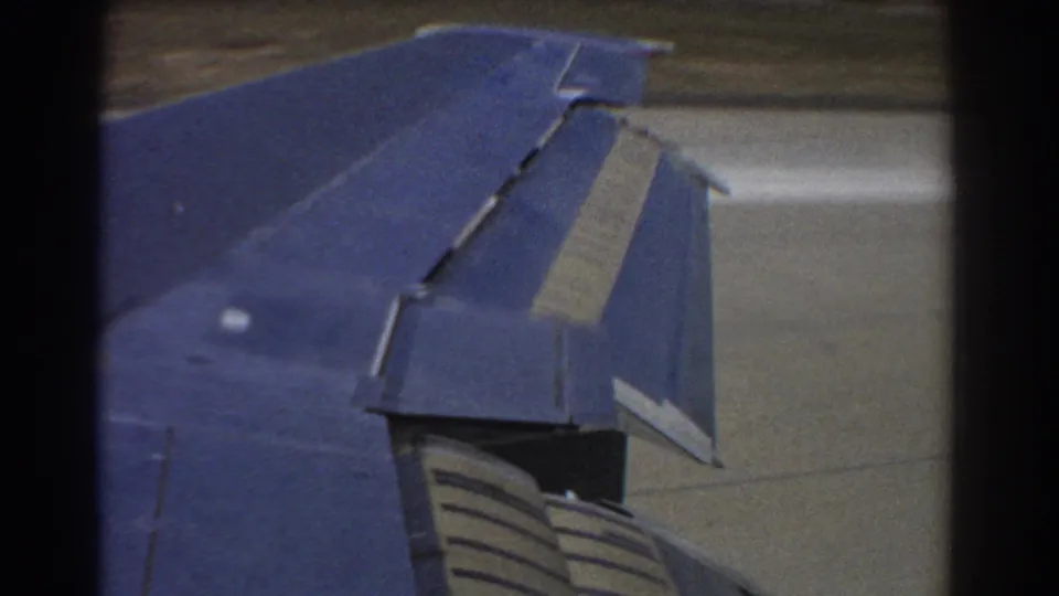 Passenger-window view of the blue airplane wing and flap assembly during runway movement in Perth, 1967.
