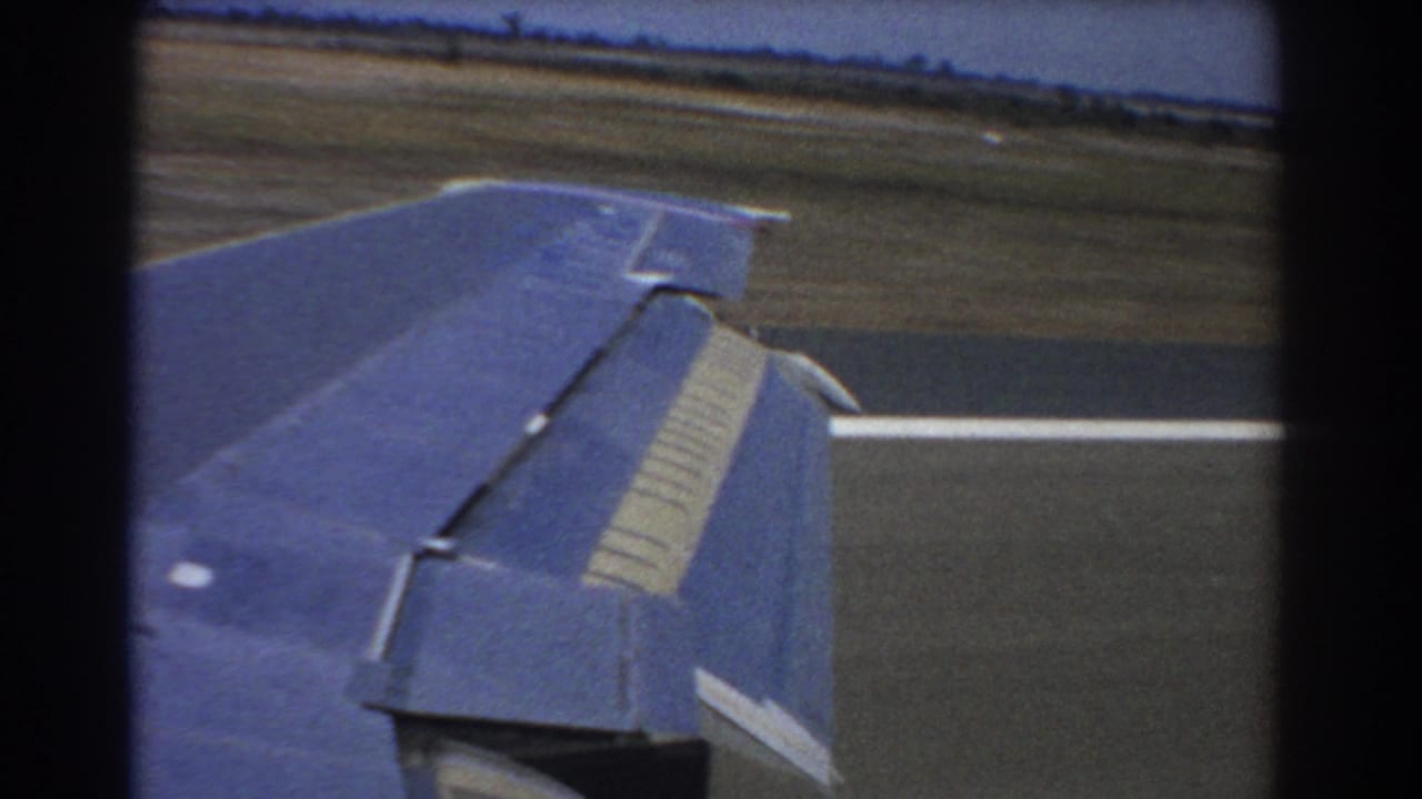 Airplane wing seen from a passenger window while taxiing beside runway pavement and grass.