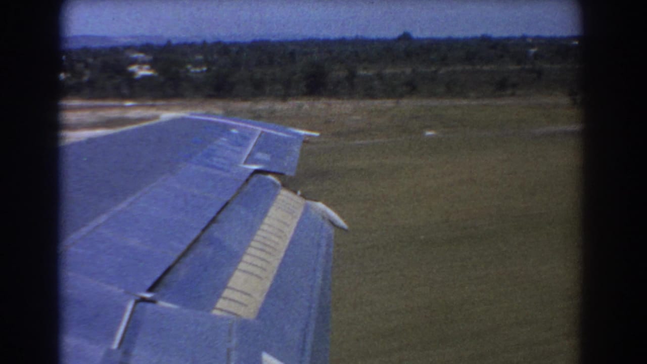 Aircraft wing passes above grass with runway curve nearby.