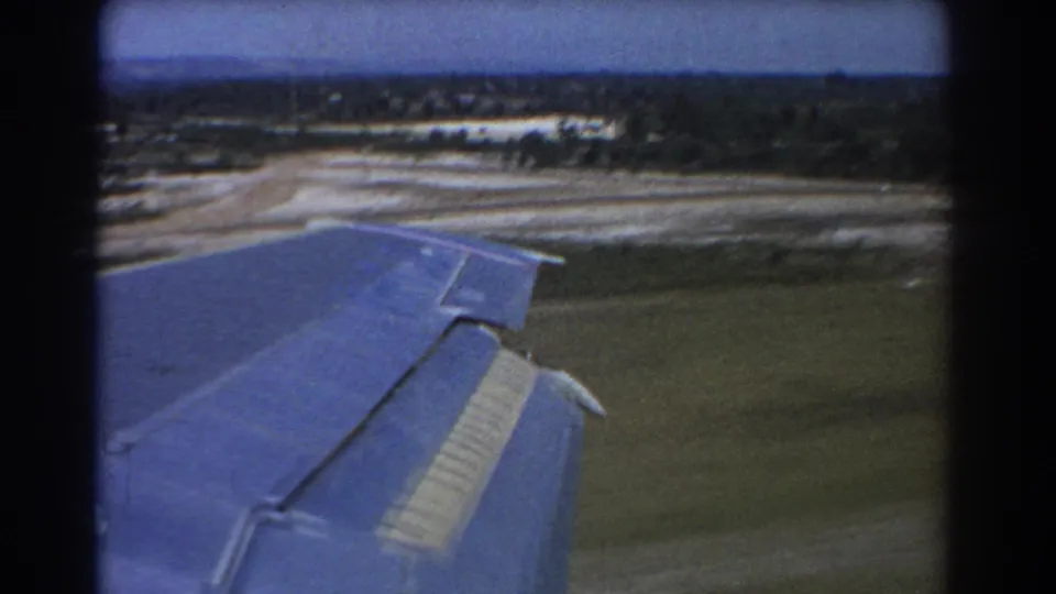 1967 8mm passenger view of an aircraft wing over blurred grass and light runway areas during takeoff in Perth.