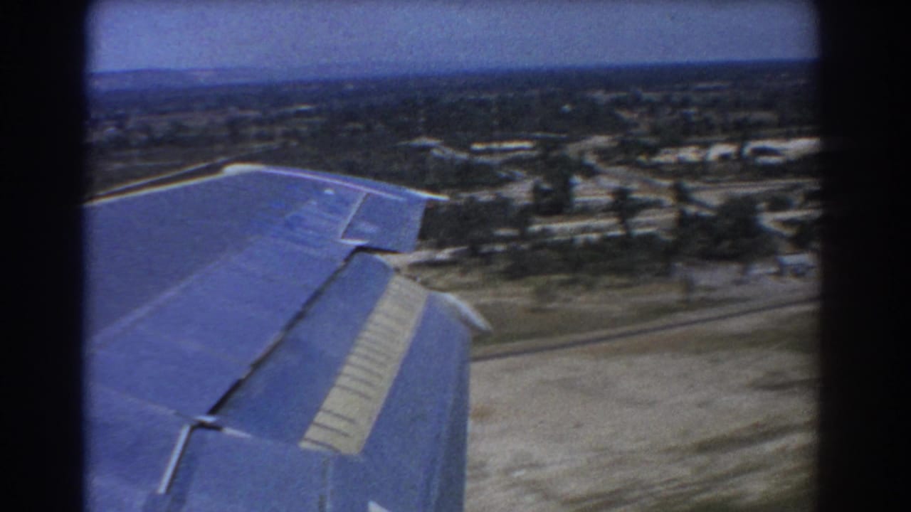 Aircraft wing above roads, trees and low buildings near landing.