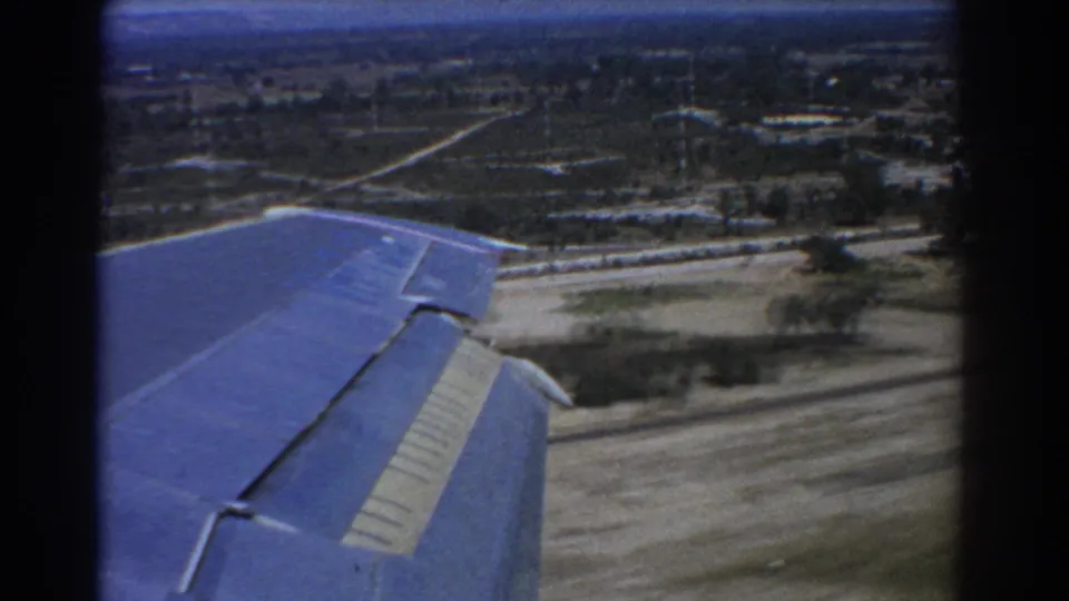 1967 Perth-area frame showing the aircraft wing passing above cleared ground, a road and sparse buildings during the landing approach.