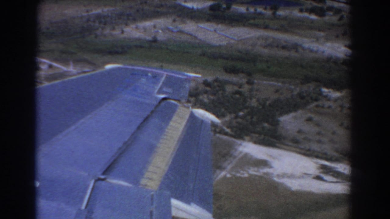 Airplane wing over fields, roads, and a small cluster of rural structures.