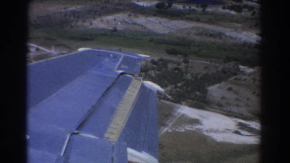 Passenger-window view near Perth in 1967, with the blue wing crossing above fields, roads, trees, and distant structures.