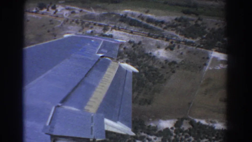 Final 1967 Perth aerial frame with the blue aircraft wing in foreground and rural fields, tracks, and trees below.