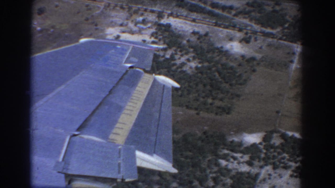 1967 Perth-area airplane-window view with a blue wing in the foreground and open fields below.