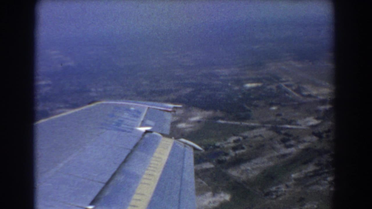 Aircraft wing over hazy farmland and roads viewed from above.