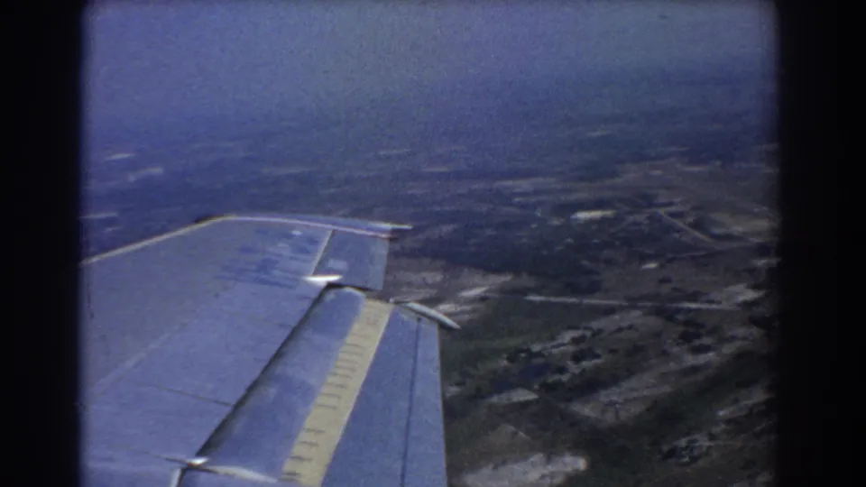 Soft 8mm frame of a plane wing over Perth-area farmland, with roads and structures visible through motion and haze.