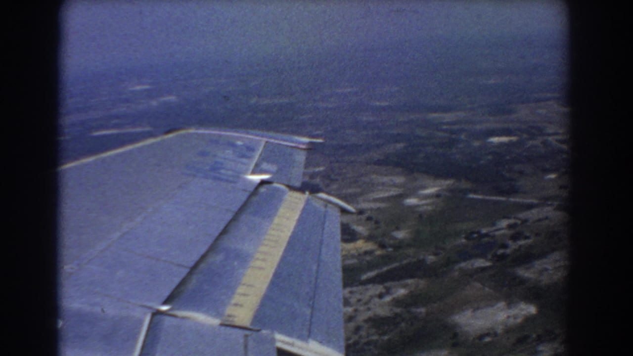Airplane wing over hazy rural terrain seen from a passenger window.