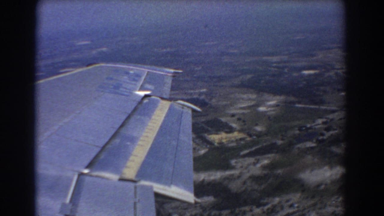 Airplane wing fills the foreground above fields and scattered settlement below.