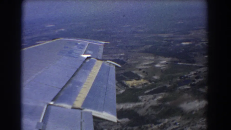 Passenger-window view from a 1967 8mm travel film, with airplane wing foreground and rural land below near Perth.
