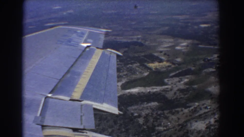 1967 8mm airplane-window shot over rural terrain near Perth, with wing, stripe, roads, trees, and open land visible.