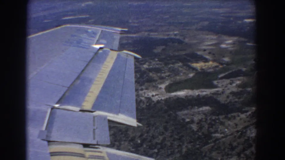 End-frame passenger view from 1967 8mm footage near Perth, showing the aircraft wing above a broad rural landscape.