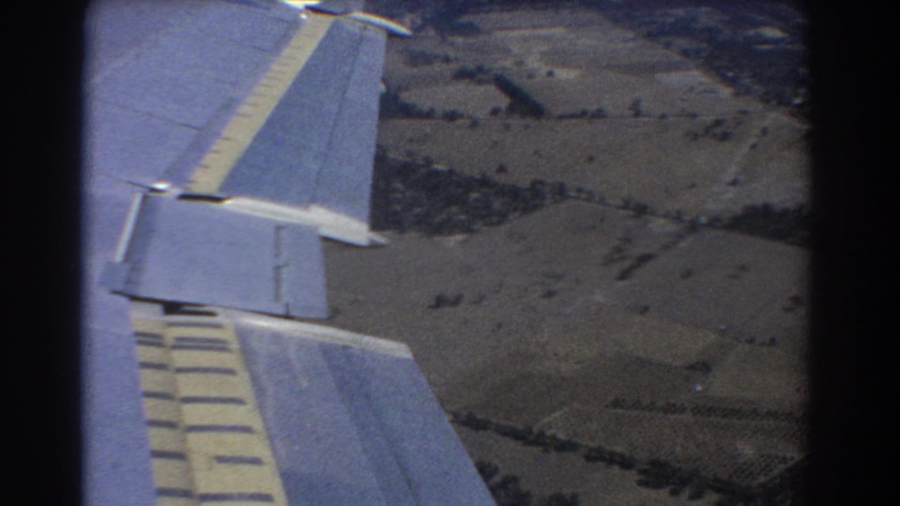 Airplane wing seen from a passenger window over rural farmland.