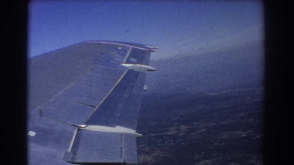 Final passenger-window view from the 1967 Perth flight clip, with the aircraft wing set against sky and distant haze.