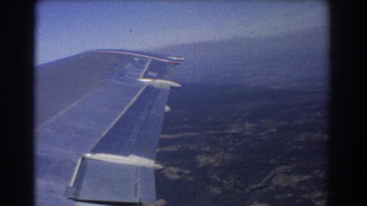Airplane wing stretches across the frame with distant land and haze below.