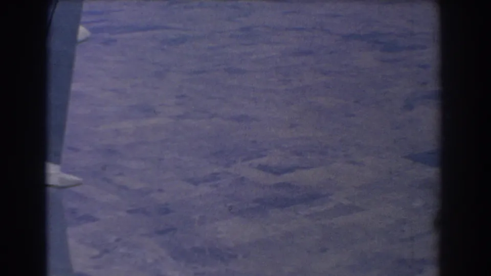 Late frame from the flight view, showing the aircraft wing at left and hazy land patterns below.