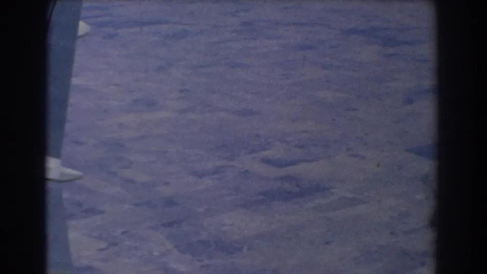 1967 8mm aerial view near Perth, Australia, looking past an airplane window frame toward hazy land below.