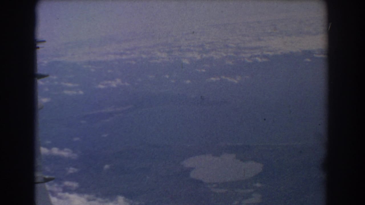 Aerial view over land and water with a pale lake visible below.