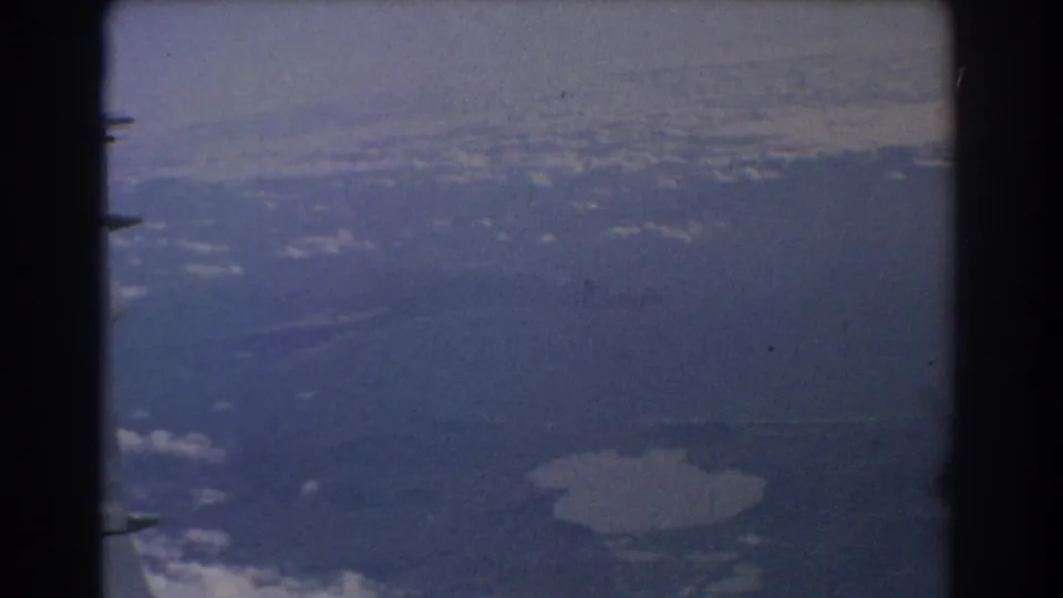 1967 8mm airplane-window view near Perth with distant terrain, cloud haze, and a pale lake shape below.