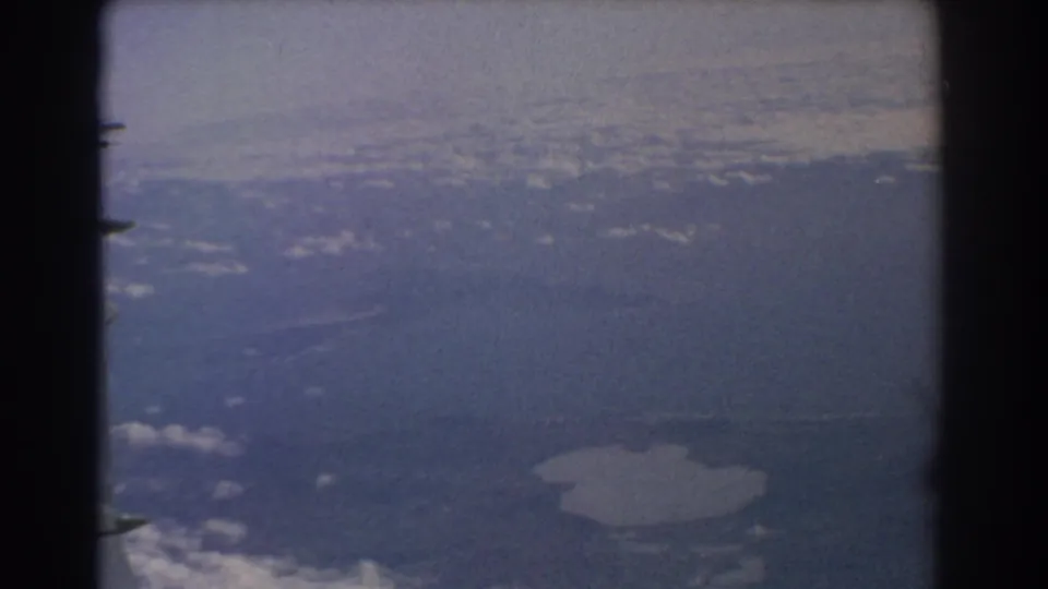 1967 8mm passenger-window shot near Perth with aircraft structure in silhouette and a pale lake below.