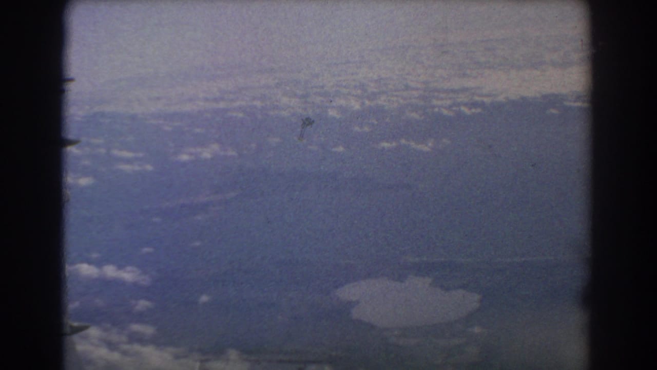 Aerial view through a film frame with distant land or water and a pale sky.