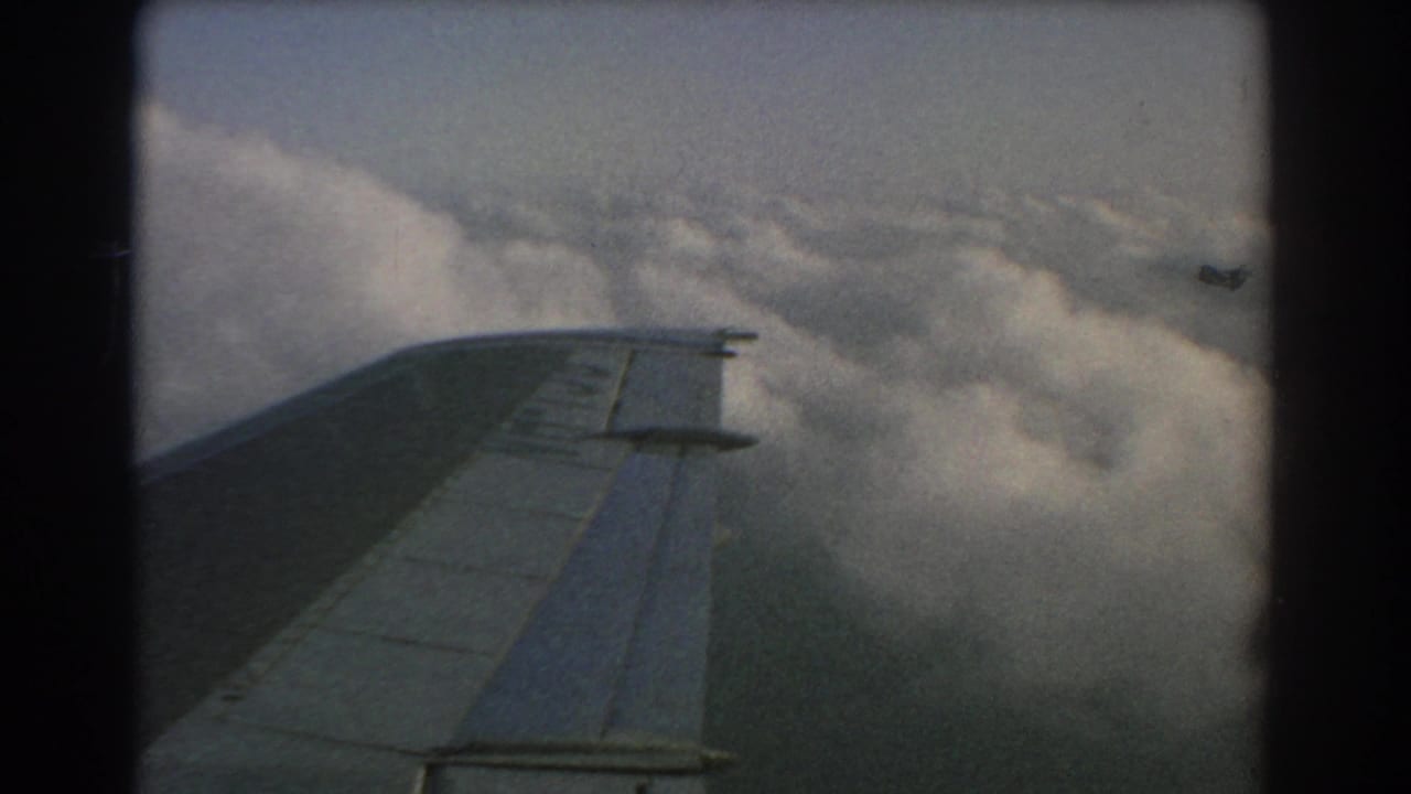 Airplane wing seen above thick clouds through a dark-edged film frame.