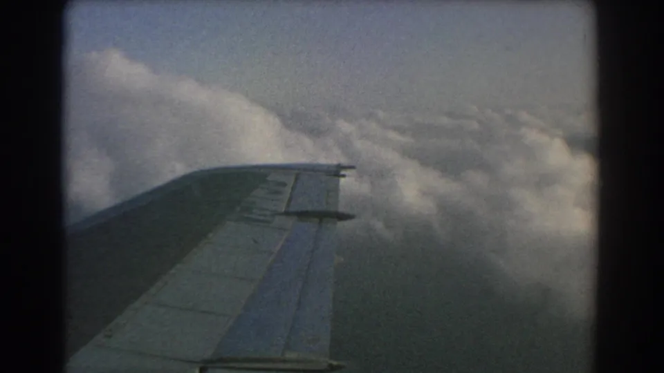 1967 8mm airplane-window view near Perth, Australia, showing the wing over dense cloud cover in soft faded color.