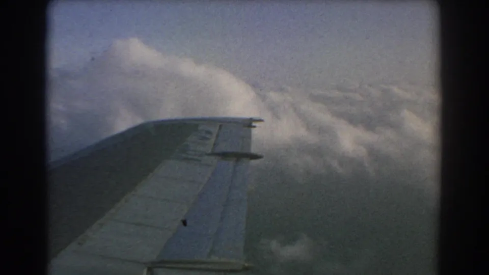 1967 8mm passenger-shot frame over Perth, Australia, with the aircraft wing set against bright clouds and open sky.