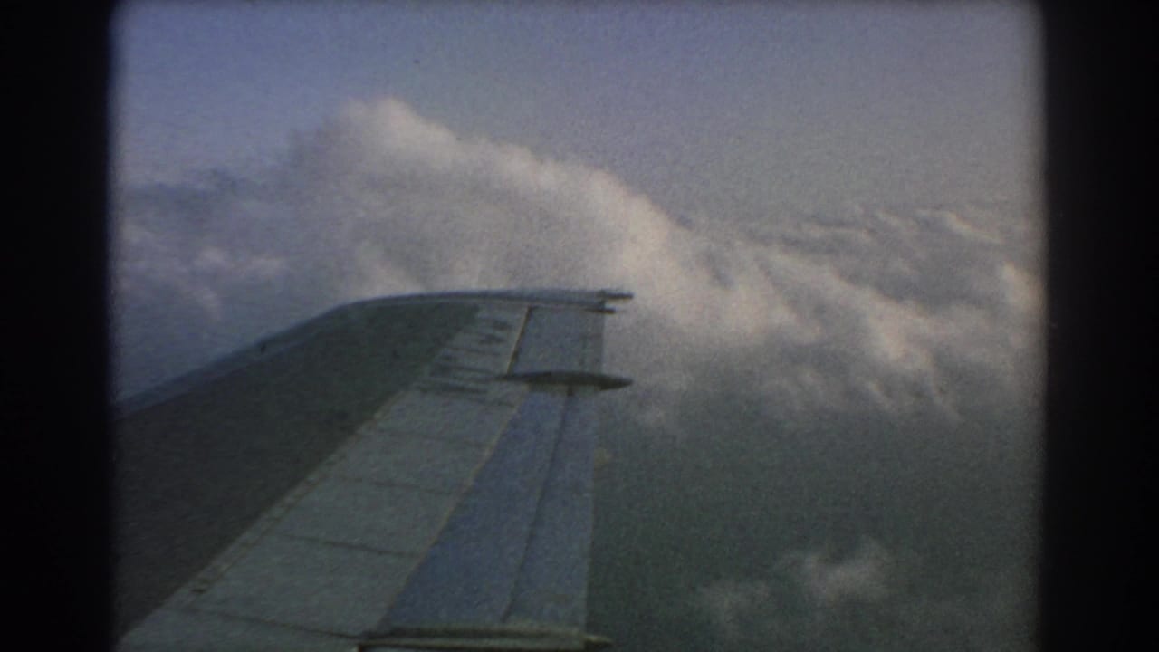 1967 8mm home-movie view from an airplane window near Perth, showing the wing passing above dense clouds.